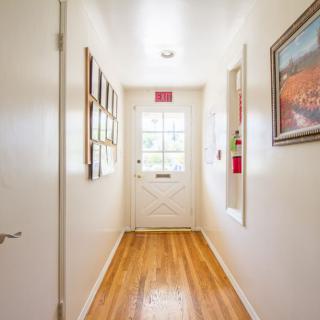 A well-lit hallway with wooden flooring and decorative paintings leading to a door.
