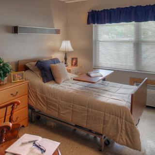 A well-lit hospital room featuring a neatly made bed, a bedside lamp, and personal touches.