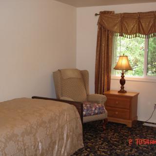 A cozy bedroom with a comfortable chair, nightstand, and lamp by the window.