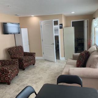 A cozy living room with chairs, a sofa, a table, and a TV mounted on the wall.