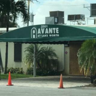 Entrance to Avante at Lake Worth with a green awning and traffic cones.