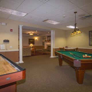 A cozy game room featuring a pool table and shuffleboard under warm lighting.