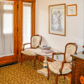 A cozy sitting area with vintage chairs and a small table, featuring wooden doors and framed artwork on the wall.