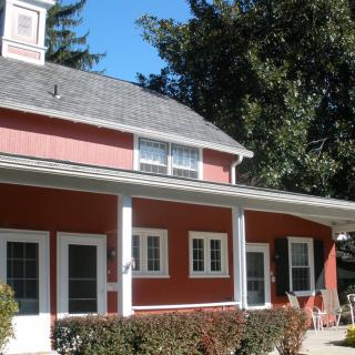 A charming red house with a porch surrounded by trees.