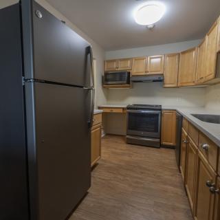 A modern kitchen with wooden cabinets, equipped with a refrigerator, stove, and microwave.