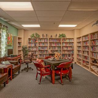 A cozy library space featuring bookshelves filled with books, a central table surrounded by chairs, and a warm atmosphere for studying and reading.