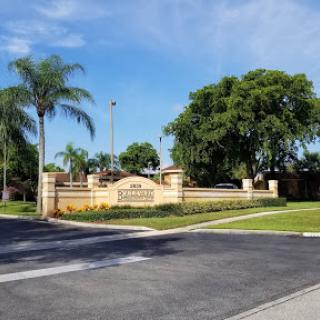 Entrance to a residential community featuring lush landscaping and palm trees.
