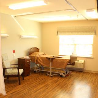 A clean and organized hospital patient room featuring a bed, chair, and natural light.