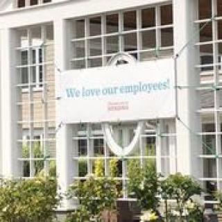 A large banner saying 'We love our employees!' displayed on the exterior of a building with numerous windows and surrounding plants.