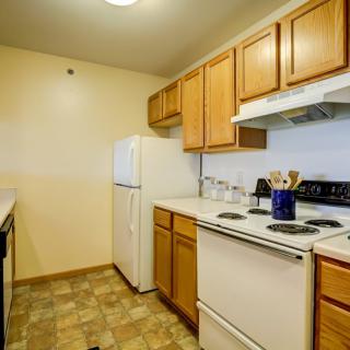 A compact kitchen featuring wooden cabinets, a stove, refrigerator, and white countertops.