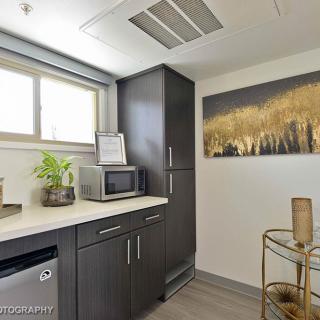A modern kitchen with sleek dark cabinets, a microwave, and refrigerator, decorated with artwork on the wall.