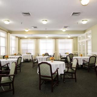 An empty dining room with tables and chairs arranged neatly, illuminated by natural light from large windows.