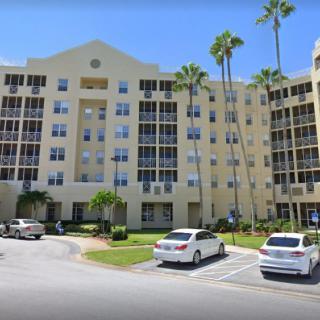 A residential apartment building with palm trees and a parking lot with parked cars.