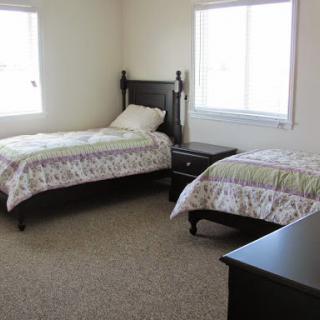A neatly arranged bedroom featuring two twin beds and a nightstand, illuminated by natural light from the windows.