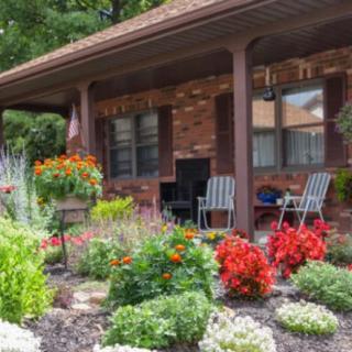A vibrant garden with blooming flowers and a cozy porch featuring chairs.