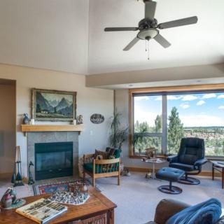 Cozy living room with a fireplace, ceiling fan, and large window offering a scenic view.