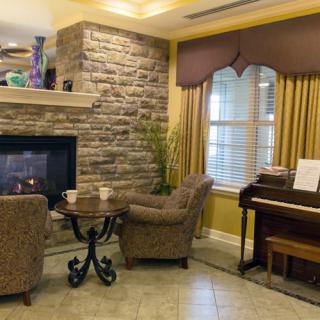 A cozy living room with a stone fireplace, two armchairs, and a piano.