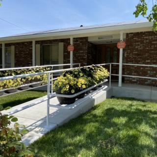A brick house with a wheelchair ramp adorned with yellow flowers and lush green grass.