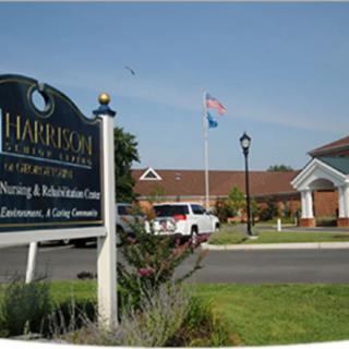 Entrance sign and view of the Harrison nursing and rehabilitation center with flags and parking area.