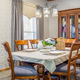 A cozy dining room with a wooden table set for a meal, accompanied by matching chairs and illuminated by a modern chandelier.