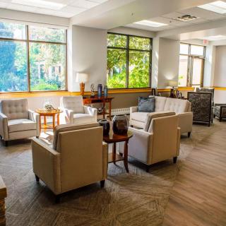 A bright and comfortable waiting room with chairs and tables arranged around large windows.