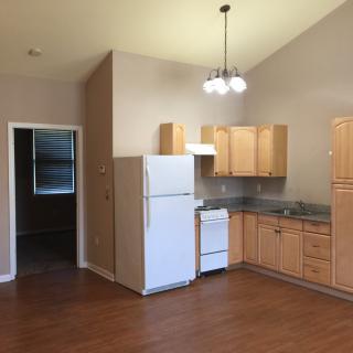A small kitchen area in an apartment featuring wooden cabinets, a fridge, and a stove.