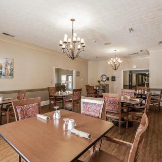 A spacious dining room with elegant chandeliers, neatly arranged tables and chairs, and a warm wooden floor.