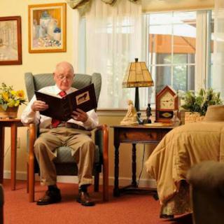An elderly man enjoys reading a book in a cozy, well-lit room.
