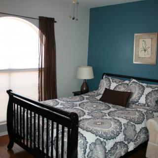 A cozy bedroom with a patterned bedspread, dark wooden bed frame, and a bedside lamp against teal and light blue walls.