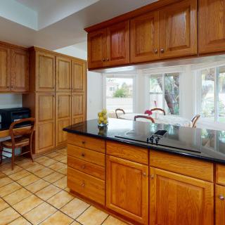 A spacious kitchen with wooden cabinets, a granite countertop island, and large windows letting in natural light.