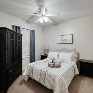 A cozy, minimalistic bedroom featuring a neatly made bed with striped bedding, a wardrobe, nightstands, and a ceiling fan.