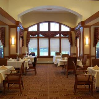 A warmly lit dining room with elegantly set tables and large windows.