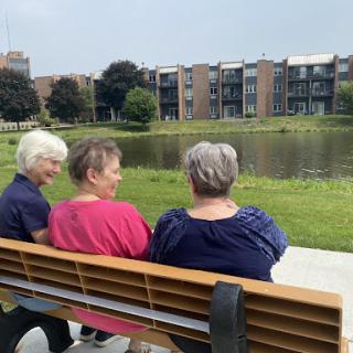 Three women enjoying a peaceful moment together by the water in a park.