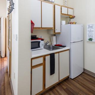 A compact apartment kitchen with essential appliances and wooden flooring.