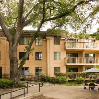 A serene residential apartment building surrounded by lush trees and featuring spacious balconies.