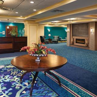A modern hotel lobby featuring a round table with a floral arrangement, comfortable seating, and a fireplace.