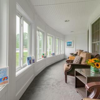 A cozy sunroom with large windows, comfortable seating, and vibrant flowers.