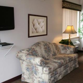 A cozy living room features a floral-patterned couch, wall-mounted television, artwork, and a lamp near a window.