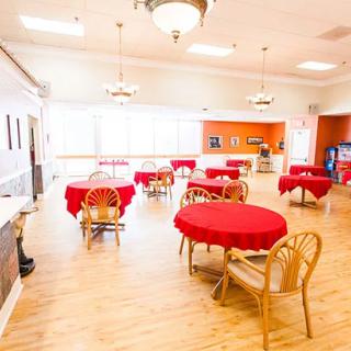 A spacious dining room with red tablecloths covering the tables and wooden chairs arranged neatly around them.