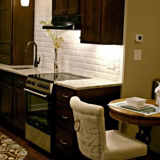 A modern kitchen with dark cabinets and a white backsplash, featuring a small dining area.