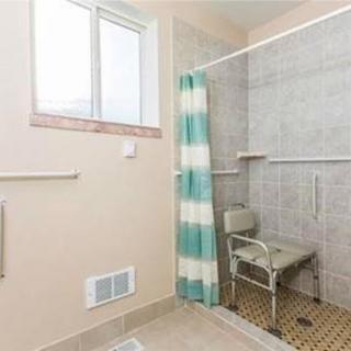 A bathroom featuring a tiled shower with a chair and striped curtain.