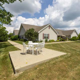 A suburban house with a patio set on a grassy lawn under a cloudy sky.
