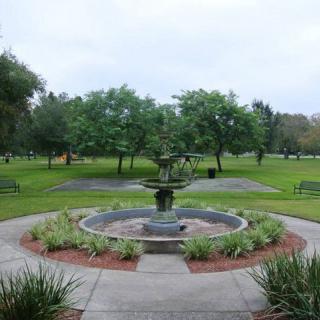 A scenic view of a fountain surrounded by lush greenery and benches in a park.