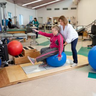 A physical therapist assisting a patient with balance exercises on a stability ball.