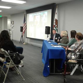 A panel discussion taking place with speakers at a table and an audience in attendance.