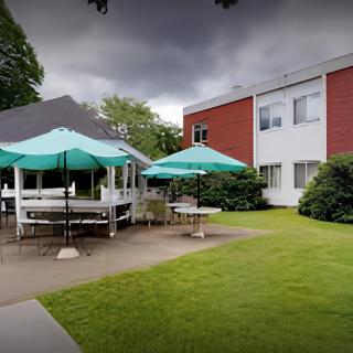A building with outdoor seating under umbrellas, surrounded by a well-maintained lawn and a cloudy sky.