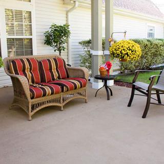A cozy porch with wicker furniture featuring striped cushions, a small table, and potted plants.