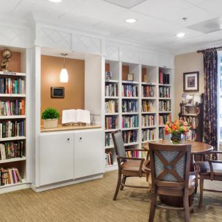 A cozy library corner with bookshelves and a round table surrounded by chairs.