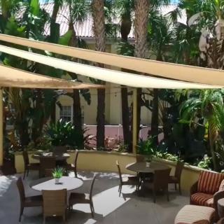 A cozy outdoor patio with seating areas, shaded by sail canopies and surrounded by tropical plants.