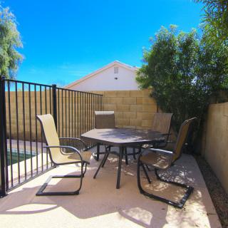 A sunny backyard patio with outdoor furniture and a fenced area.